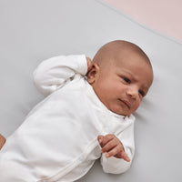 close up of sleepy newborn baby laying on a beddybyes silver grey Silk Universal Travel Slip inside a cot bed