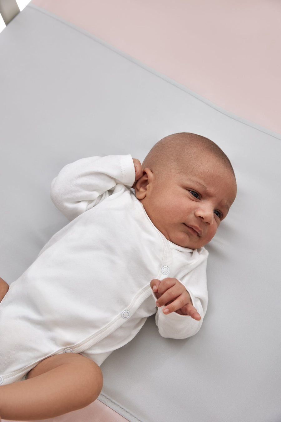 close up of sleepy newborn baby laying on a beddybyes silver grey Silk Universal Travel Slip inside a cot bed