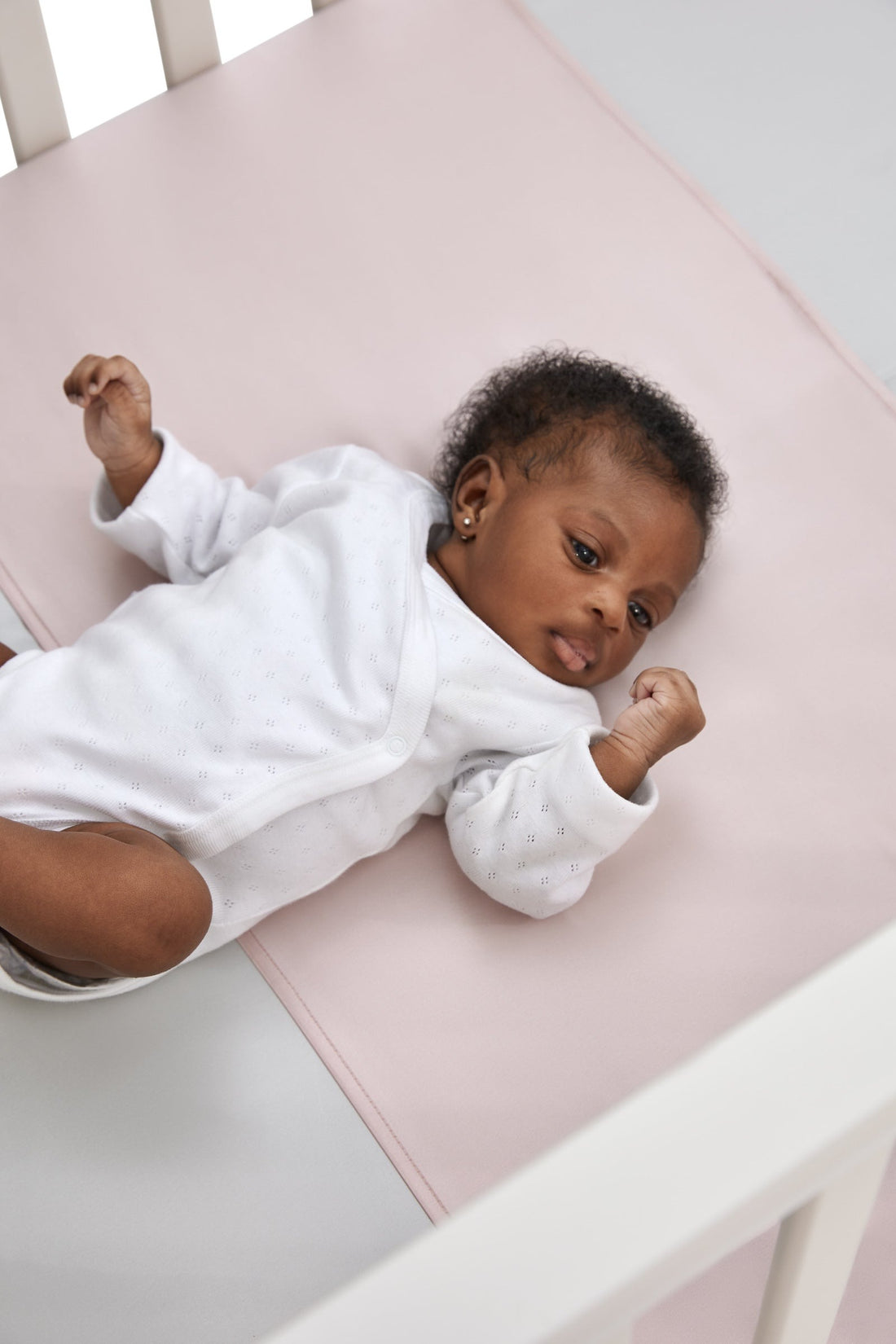 close up of gorgeous black baby girl laying on a beddybyes rose pink Silk Universal Travel Slip inside a cot bed