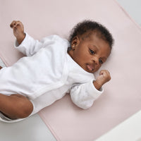 close up of gorgeous black baby girl laying on a beddybyes rose pink Silk Universal Travel Slip inside a cot bed