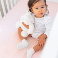 beautiful ittle girl with soft toy sitting in crib with BeddyByes Blush Pink Silk Cotbed Fitted Sheet