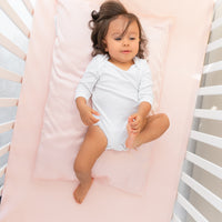 Toddler girl laying on a BeddyByes Blush Pink Silk Cotbed Fitted Sheet