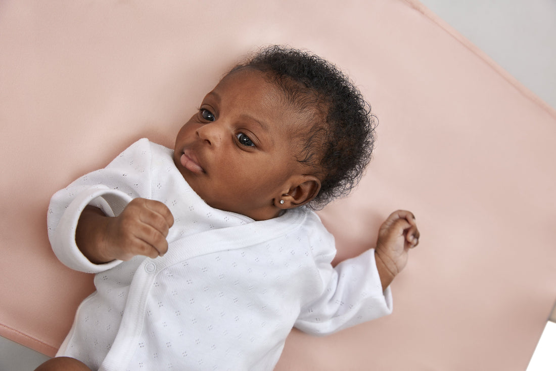 close up of gorgeous black baby girl laying on a beddybyes blush pink Silk Universal Travel Slip inside a cot bed